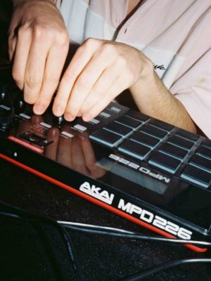 A young person using a sample and drum machine. Both of their hands are busy touching buttons on the AKAI MPD226.