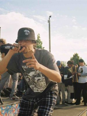 Young people performing outdoors at a skate park, holding microphones with long leads.